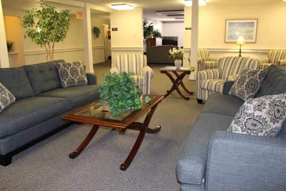 A living room with a grey couch and a coffee table with a plant on it at Greenbrier Seniors Apartments, Chesapeake, Virginia