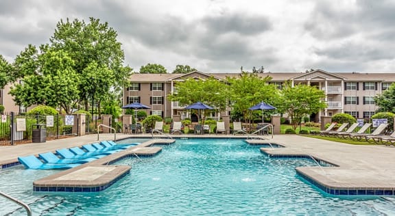 a swimming pool with chaise lounge chairs and umbrellas in front of an apartment building  at The Bristol Apartments, Greenville, 29601