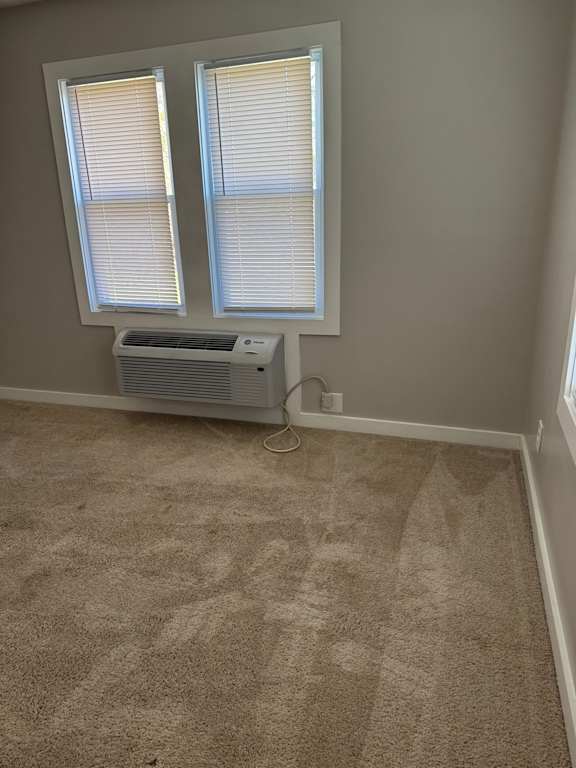 A wall-mounted air conditioner unit is on the wall next to a window.