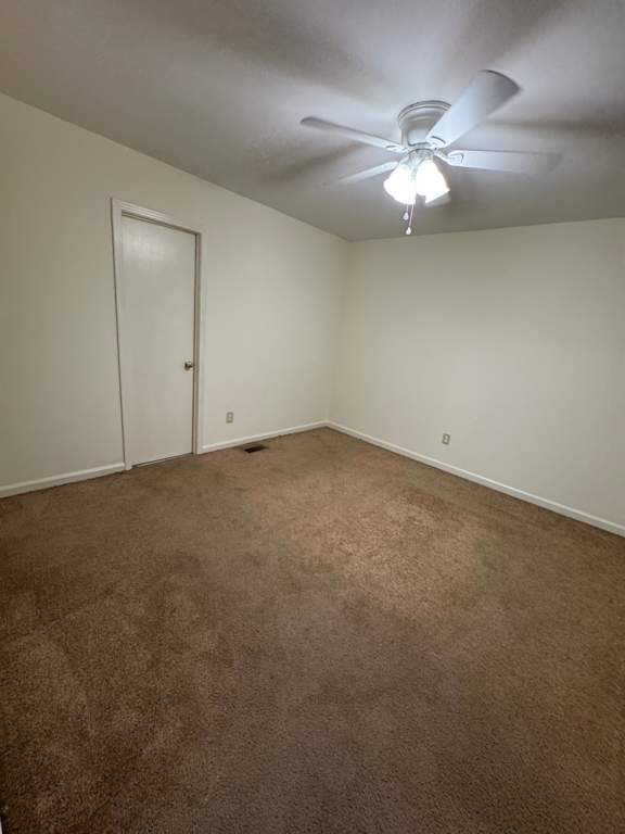 A ceiling fan with a light on in a room with a brown carpet.