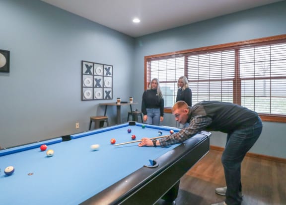 a man playing pool on a pool table in a game room with two women at Summit Ridge, Duluth, MN