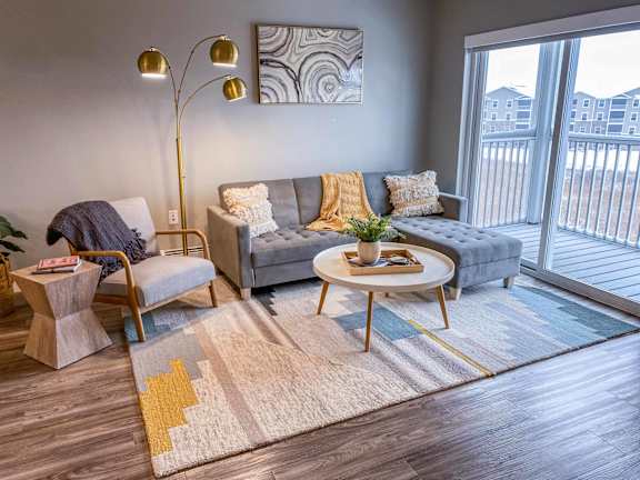 A modern living room with a grey sofa, a wooden coffee table, and a large window.