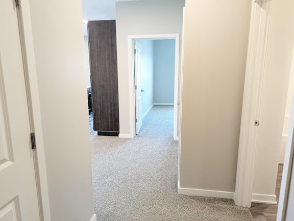 Interior hallway with carpet flooring and doorways leading to bedrooms and bathroom at Heartland Flats North Platte.