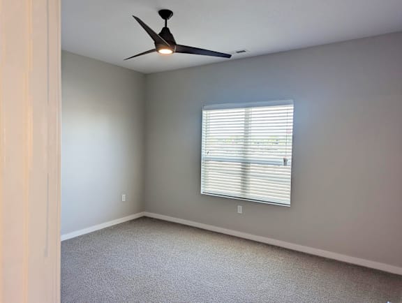 Bedroom with carpet flooring, ceiling fan, window and neutral wall colors at Heartland Flats North Platte.