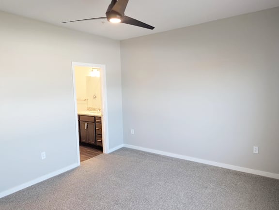 Bedroom with carpet flooring, ceiling fan and doorway leading to the bathroom at Heartland Flats North Platte.