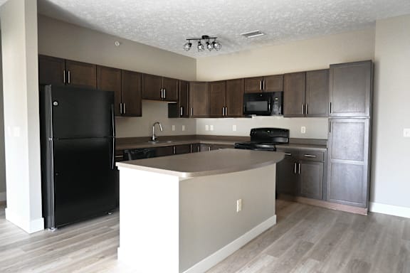 A black refrigerator stands next to a kitchen island with a microwave on top.