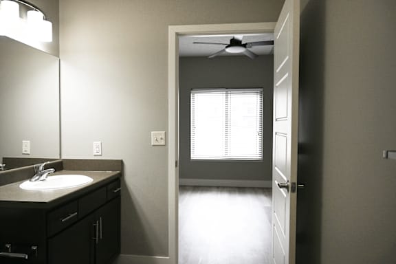 A bathroom with a sink, mirror, and a door leading to another room.