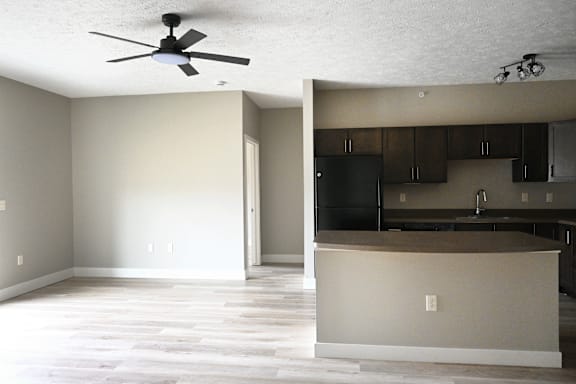 A room with a ceiling fan and a kitchen area with cabinets and a counter.