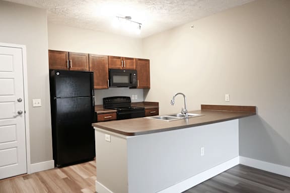 A kitchen with a black fridge and wooden cabinets.