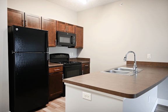 A black refrigerator is in a kitchen with brown cabinets and a black microwave.