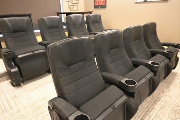 A row of black cinema seats are empty and facing the screen.