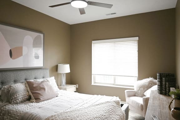 A bedroom with a large bed, a white chair, and a painting on the wall.