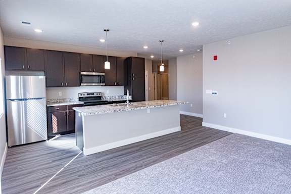 Kitchen with island seating, cabinetry, appliances and open connection to the living area at Heartland Flats Alliance.