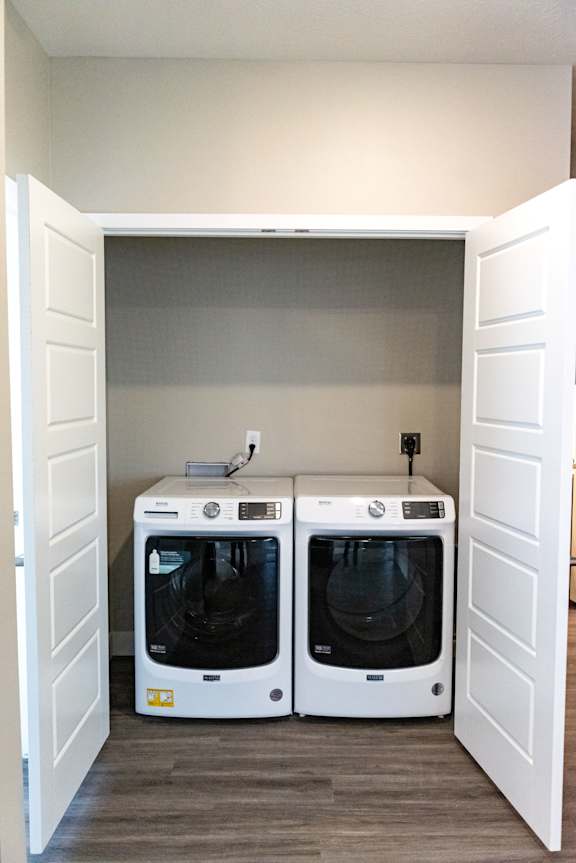 Laundry closet with side by side washer and dryer and shelving above at Heartland Flats Alliance.