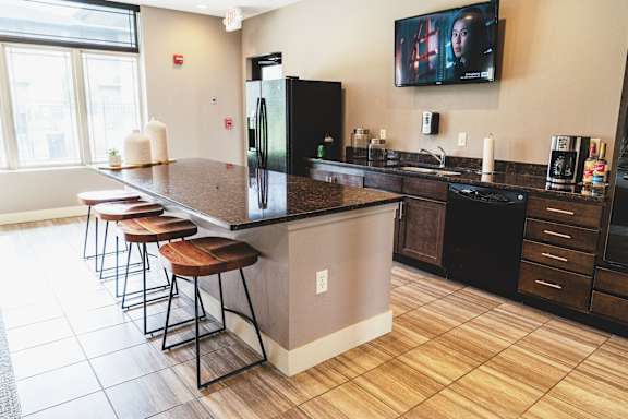A kitchen with a black fridge and a TV mounted on the wall.