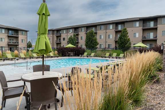 A pool area with chairs and umbrellas in front of apartment buildings.