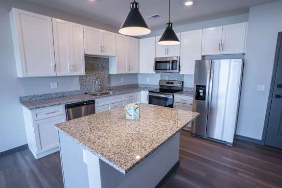 Close view of the kitchen island with pendant lights and stainless appliances behind at The Harbor.