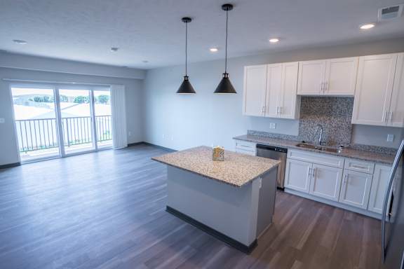 Kitchen island with pendant lights and wood style flooring extending into the living area at The Harbor.