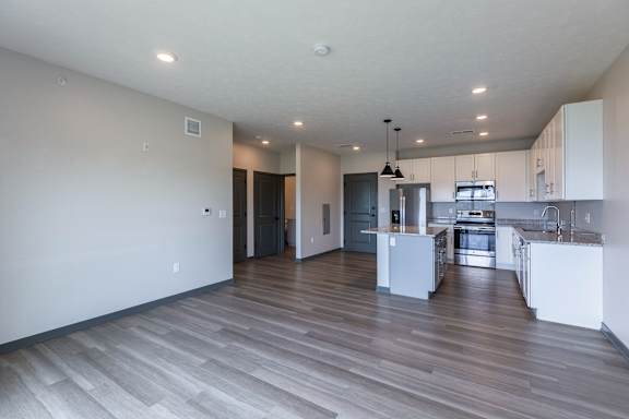 Open living room with wood style flooring leading into the kitchen and island at The Harbor.