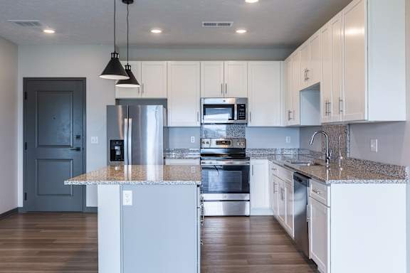 Modern kitchen with white cabinets, stainless steel appliances, an island and pendant lights at The Harbor.