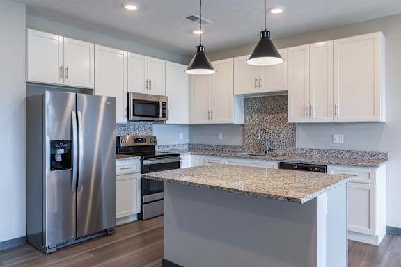 Corner view of kitchen with refrigerator, white cabinets, island and pendant lights at The Harbor.
