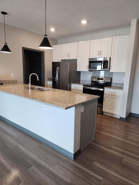 Kitchen with light cabinetry, island, pendant lights and stainless steel appliances at The Harbor.