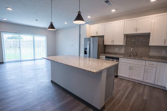 Kitchen island with pendant lighting, white cabinetry and wood style flooring at The Harbor.