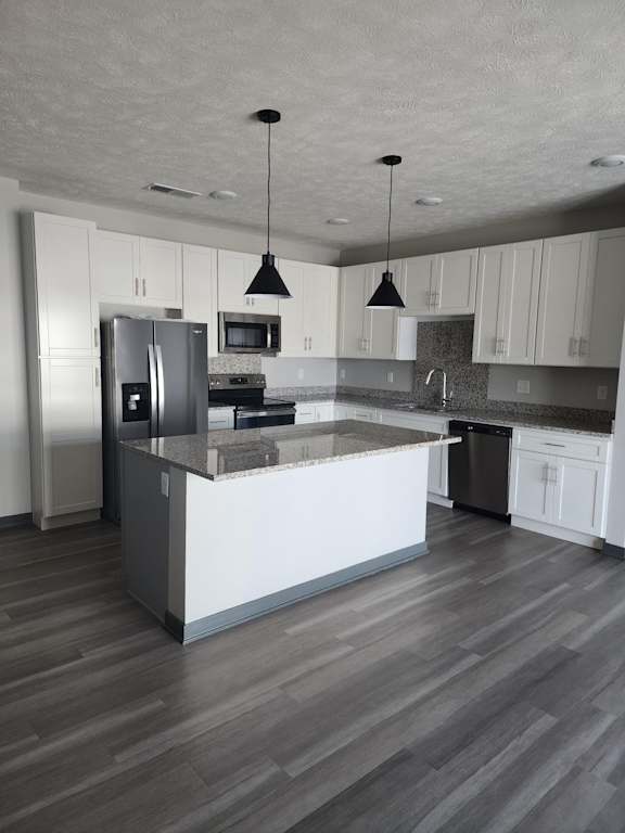 Kitchen with pendant lighting, island, stainless steel appliances and wood style flooring at The Harbor.