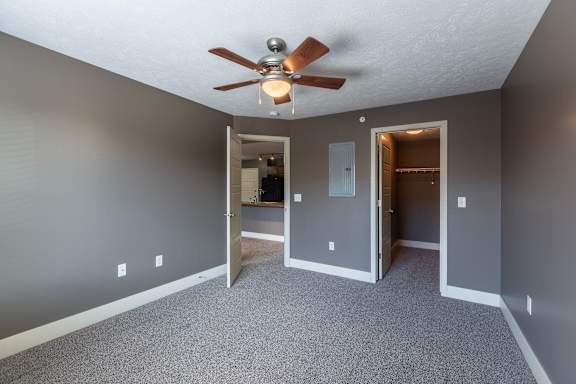 A carpeted bedroom with a ceiling fan and double-door closet in the Coventry home at The Sterling at Grand Island.