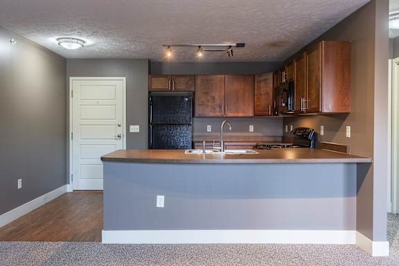 A view of the Durham kitchen with wood cabinetry and a peninsula overlooking the living area at The Sterling at Grand Island.