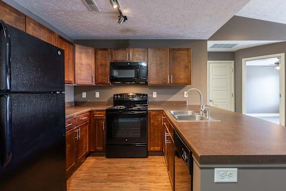 A kitchen with wooden cabinets, a black range, and overhead lighting in the Durham home at The Sterling at Grand Island.
