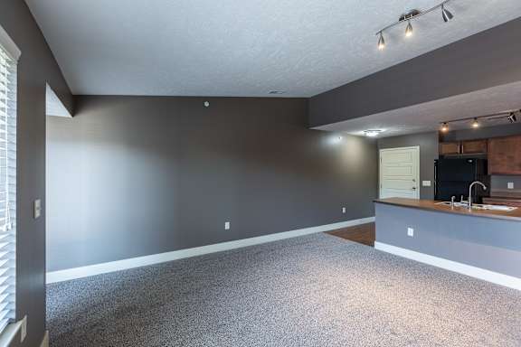 A carpeted living room with neutral paint and open layout in the Durham home at The Sterling at Grand Island.