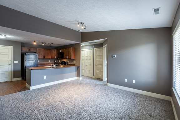 A carpeted living room with a view into the kitchen area in the Durham home at The Sterling at Grand Island.