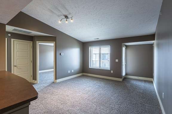 A carpeted living room with neutral walls and a wide window in the Durham home at The Sterling at Grand Island.