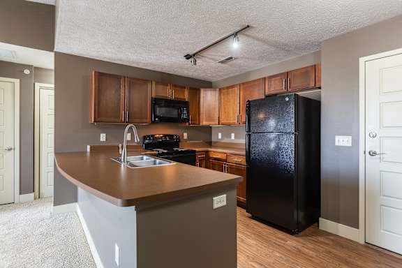 A view of the kitchen with wood cabinets, black appliances, and an island in the Kingston Garden Level home at The Sterling at Grand Island.
