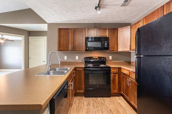 A kitchen with black appliances and wooden cabinets in the Kingston Garden Level home at The Sterling at Grand Island.