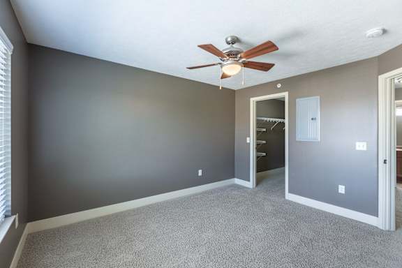 A carpeted bedroom with a ceiling fan in the Manchester ADA home at The Sterling at Grand Island.