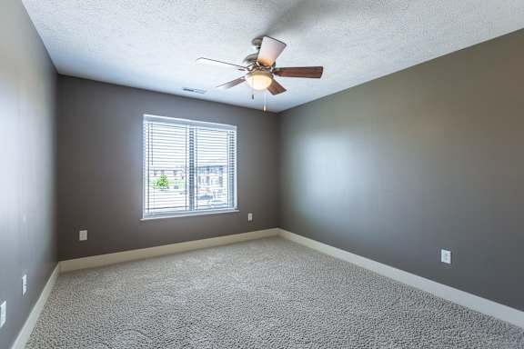 A carpeted bedroom with a window providing natural light in the Manchester ADA home at The Sterling at Grand Island.