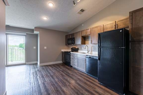 Kitchen with wood cabinets black appliances and wood flooring connected to the living area