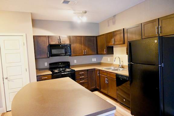 Corner kitchen with wood cabinets and black appliances at The Sterling at Kearney