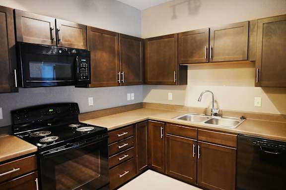 Kitchen with wood cabinets black appliances and corner countertop at The Sterling at Kearney