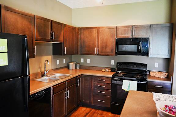 Corner kitchen with wood cabinets and black appliances at The Sterling at Kearney