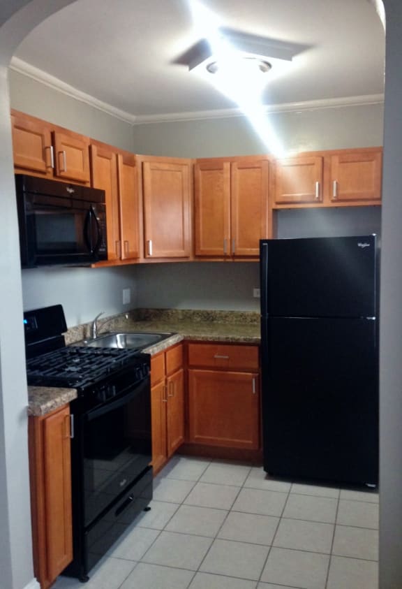 Efficient layout meets modern charm — this galley-style kitchen features full-size black appliances, natural wood cabinetry, granite-look countertops