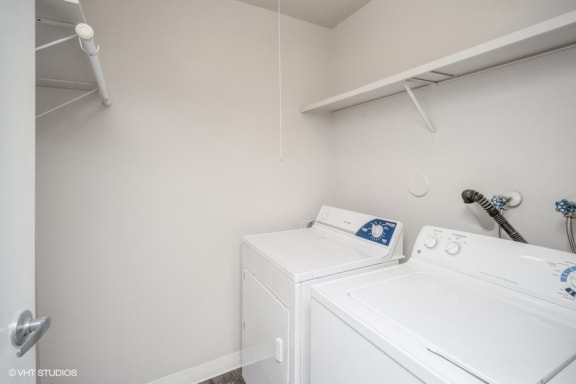 a white washer and dryer in a white room with a shelf above it