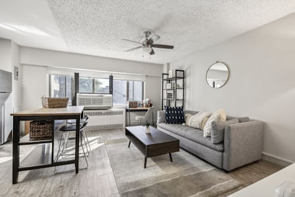 A living room with a grey couch, a wooden table, and a ceiling fan.