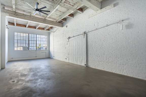 A large empty room with a ceiling fan and a window.