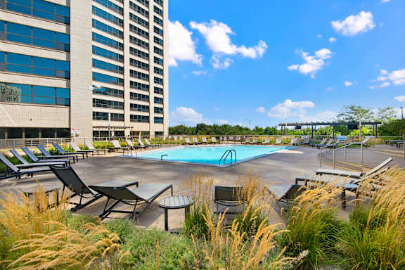 A pool surrounded by chairs and tall grass.