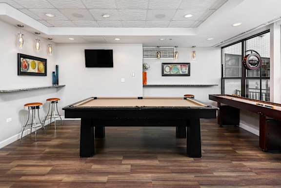 A pool table is in the middle of a room with a TV and picture frames on the wall.