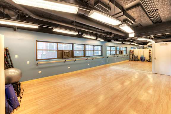 A spacious room with wooden floors and a row of windows on the wall.