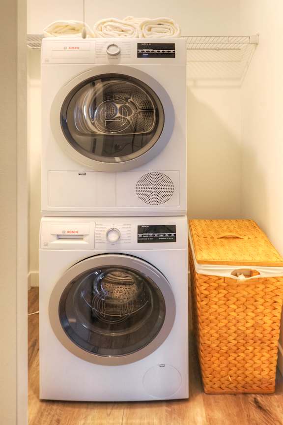 A white washing machine and dryer stacked on top of each other with a yellow laundry basket to the side.